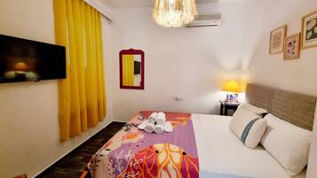 Una habitación de hotel con cama, televisión, espejo, lámpara y ventilador de techo.
