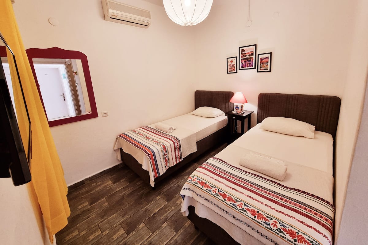 Una habitación con dos camas individuales, una mesita de noche pequeña con lámpara, aire acondicionado montado en la pared y una puerta con espejo.