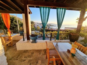 A covered outdoor seating area with a table and chairs, potted plants, and a view of a coastal town. - Kumbahçe Fethiye Hanım Pansiyon Bodrum (Bodrum)