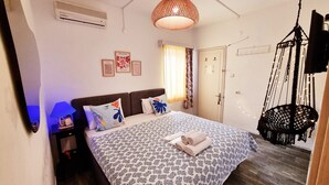 Un dormitorio con una colcha estampada, un sillón colgante de macramé y un ventilador de techo.