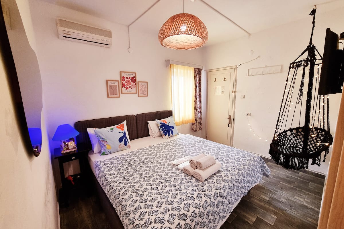Un dormitorio con una colcha estampada, un sillón colgante de macramé y un ventilador de techo.