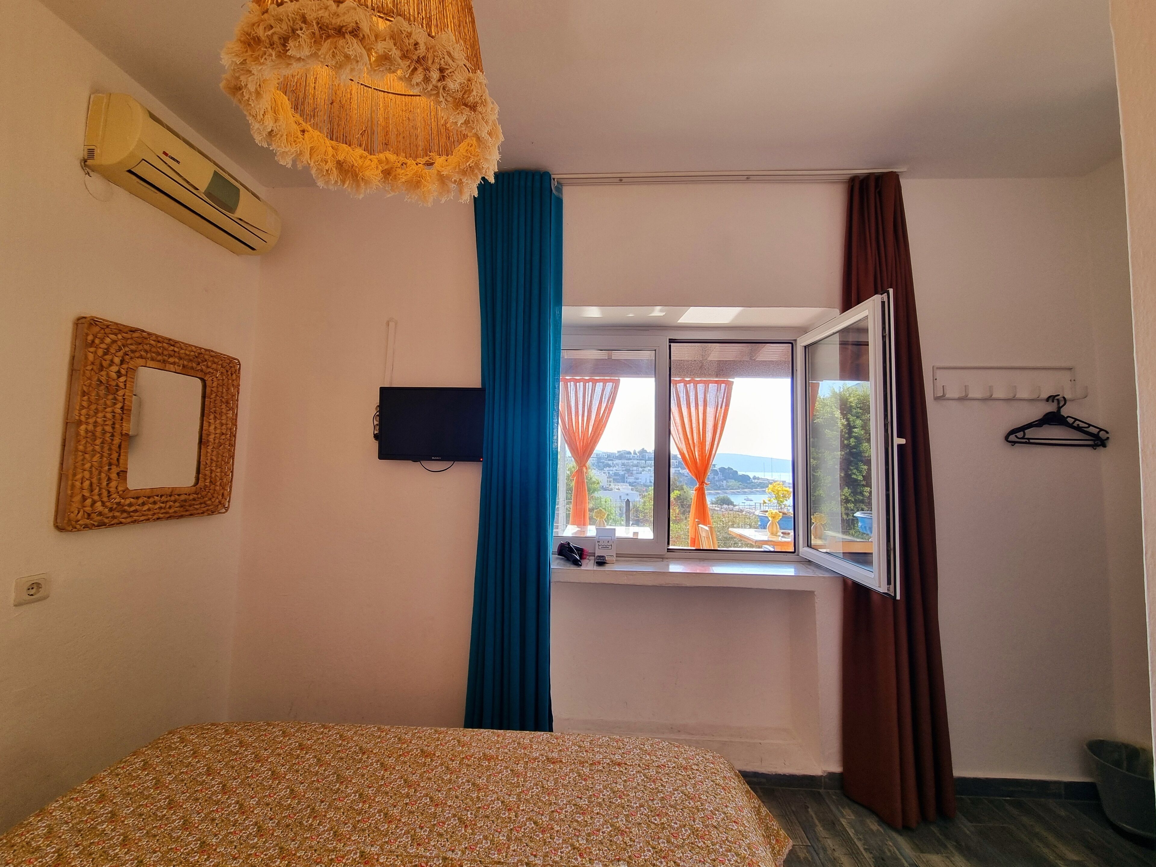 Quarto com cama, televisão, janela com cortinas e ar condicionado.