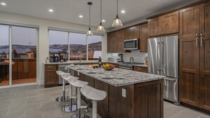 Une cuisine moderne dotée d’un grand îlot central, d’appareils électroménagers en acier inoxydable, de meubles de rangement en bois et offrant une vue sur les montagnes.
