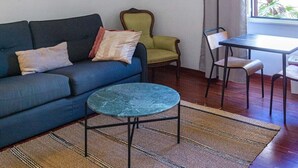 A living room with a sofa, a small round table, a green armchair, and a dining table with chairs. There is a large mirror on the wall and a chandelier with multiple light bulbs. - Colosseum Cosy Apartment Close To Metro (Rome)