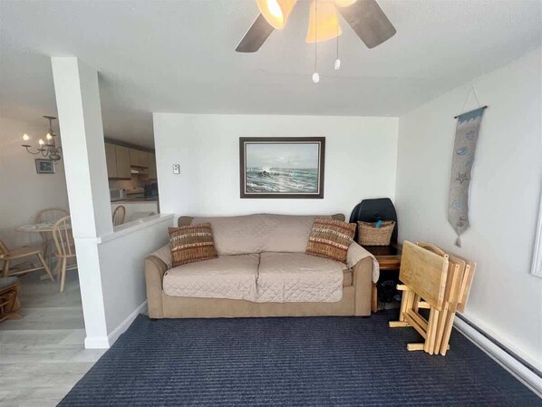 A living room with a beige sofa, a ceiling fan, a framed picture on the wall, and a small wooden table. - Oceanfront Wells Beach Condo - Ocean Surf #5 (Wells)