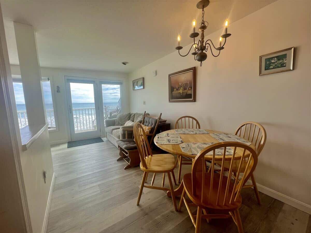A dining area with a wooden table and chairs, a chandelier, and a view of the balcony.