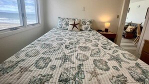 A bedroom with a large bed, a starfish pillow, and a view of the ocean through a window. - Oceanfront Wells Beach Condo - Ocean Surf #5 (Wells)
