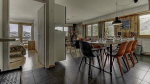 A modern dining area with a large table, chairs, and a view of the mountains through large windows. - Appartement Mont Parrain 4 - La Tzoumaz, 4 Vallees (La Tzoumaz)