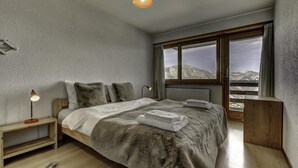 A bedroom with a large bed, a nightstand, a lamp, and a view of mountains through the window. - Appartement Mont Parrain 4 - La Tzoumaz, 4 Vallees (La Tzoumaz)