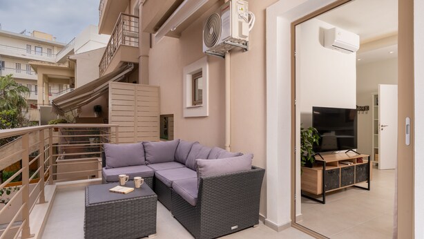 A balcony with a grey wicker sofa, a small table, and a potted plant. - Harbour Hill Suite 4—200 m. away from the beach (Rethymno)