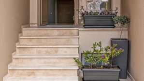 A set of beige stairs leading to a door with a window. There are two planters with plants on the landing. - Harbour Hill Suite 4—200 m. away from the beach (Rethymno)