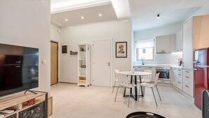 A modern living room with a flat-screen TV, a dining area with a white table and chairs, and a kitchen with white cabinets and a red refrigerator. - Harbour Hill Suite 4—200 m. away from the beach (Rethymno)