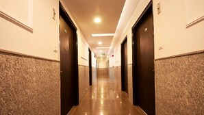 A long, narrow hallway with dark wooden doors on both sides, leading to a bright exit at the end.