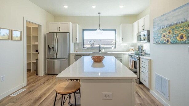 Una cocina moderna con armarios blancos, una isla grande, electrodomésticos de acero inoxidable y vistas al exterior.