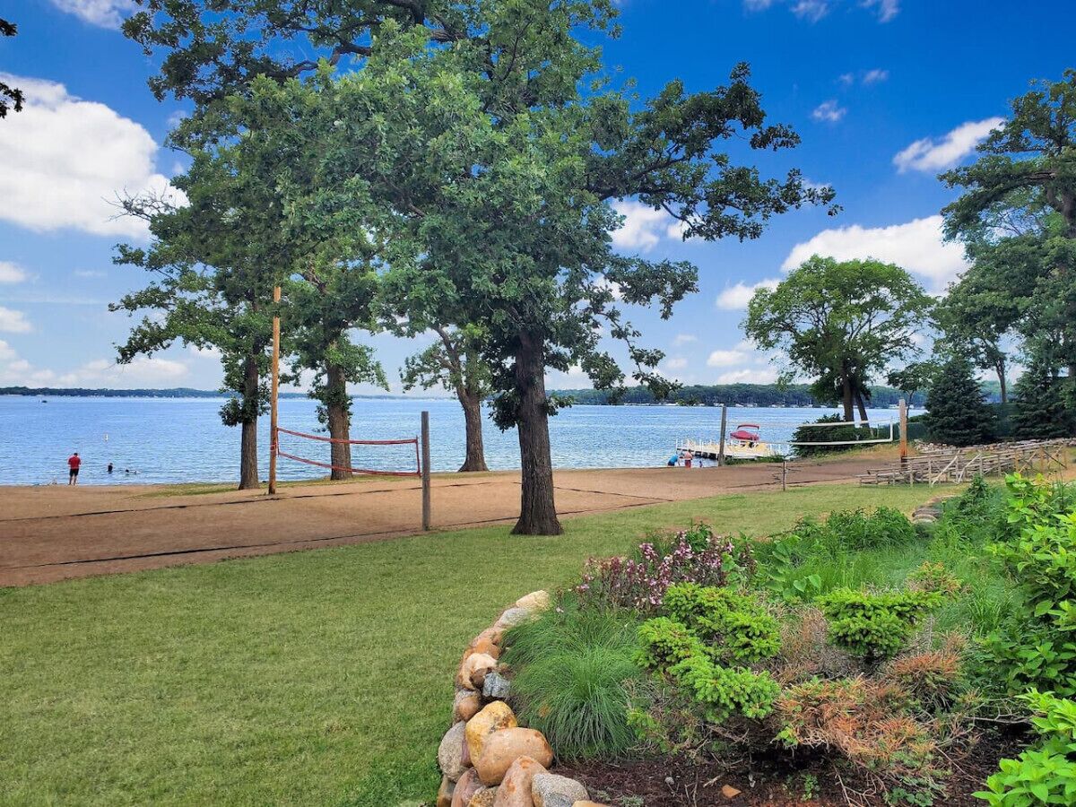 A beach volleyball court with a net, trees, and a lake in the background.