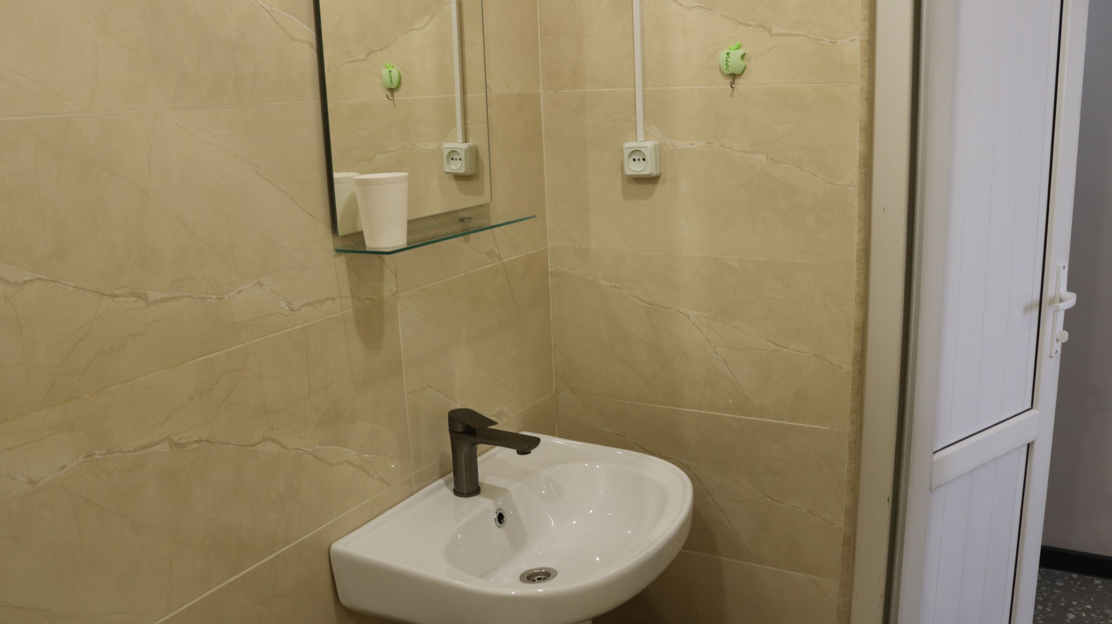 A bathroom with a white sink, a mirror, and two electrical outlets on the wall.