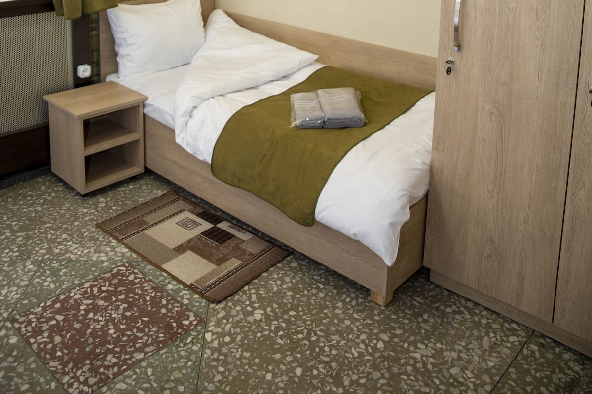 A neatly arranged hotel room with a bed, a wooden wardrobe, a small bedside table, and a window with curtains.