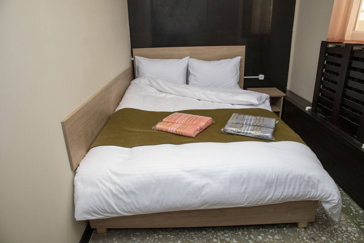 A neatly made bed with white linens, a green throw blanket, and two folded towels.