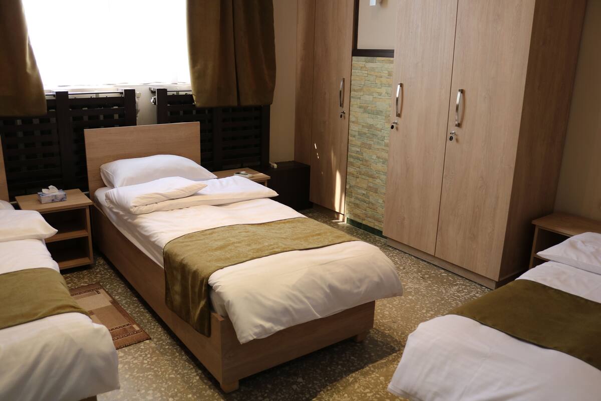 A hotel room with a large bed, a wardrobe, a bedside table, and a window with curtains.