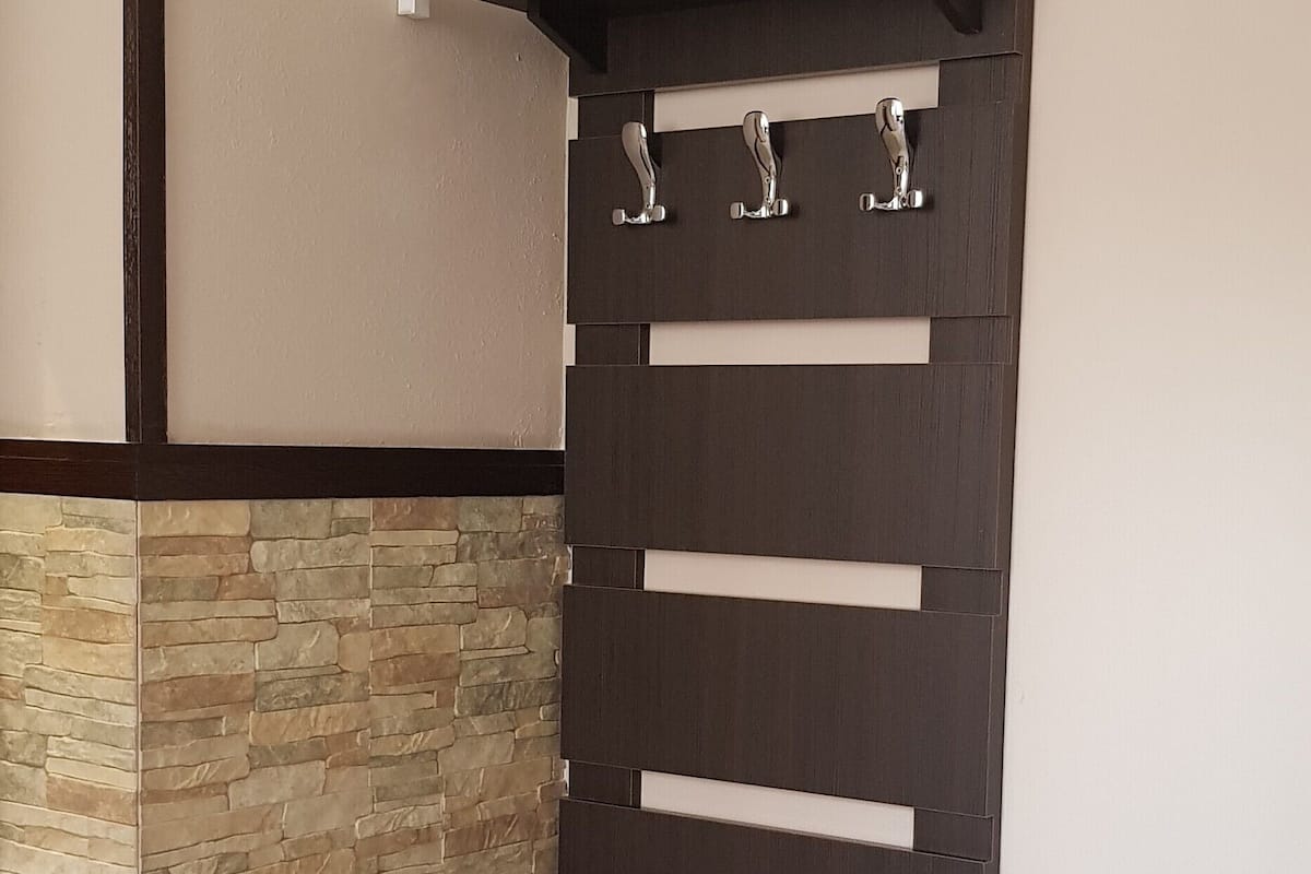 A bedroom with a bed, a stone accent wall, a dark wooden shelf with hooks, and a small wooden nightstand.