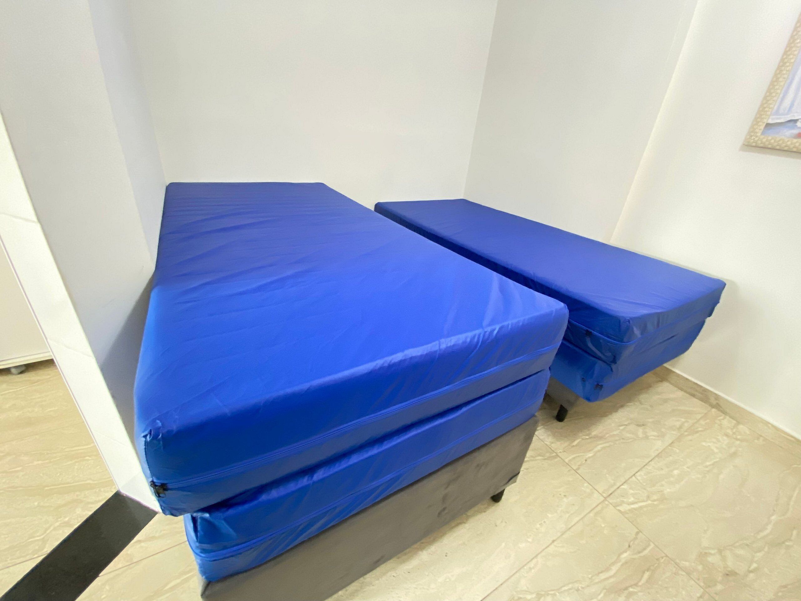 Une pièce avec deux lits recouverts de draps bleus, un sol carrelé et un mur blanc.