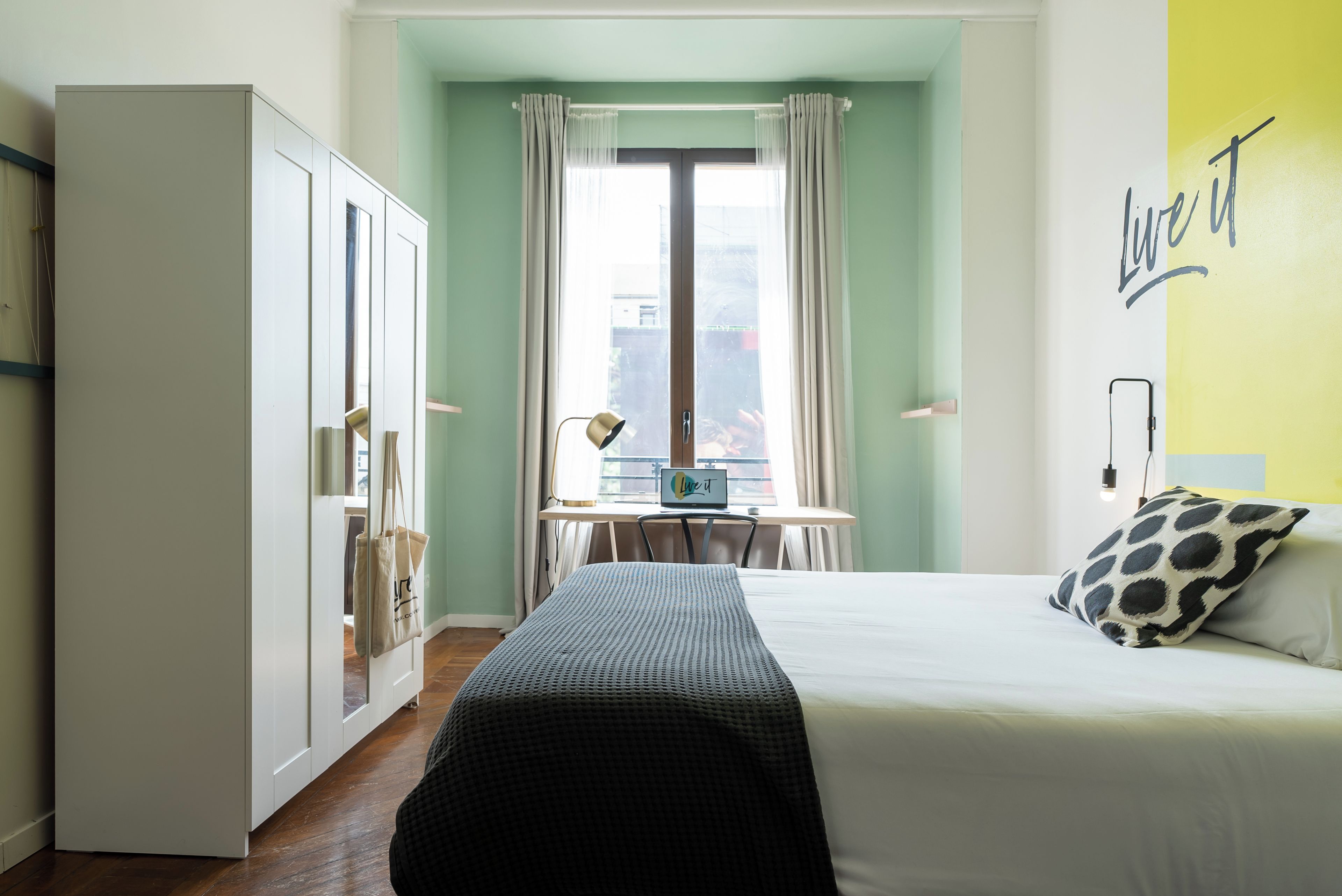 Ein Hotelzimmer mit Bett, Schreibtisch, Kleiderschrank und Blick auf die Stadt.