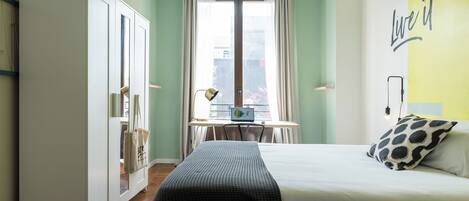 A hotel room with a bed, a desk, a wardrobe, and a view of the city.