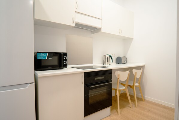 A modern kitchen with white cabinets, a microwave, a coffee maker, and a toaster. There are two wooden chairs and an oven. - Live It Gran Via (Madrid)