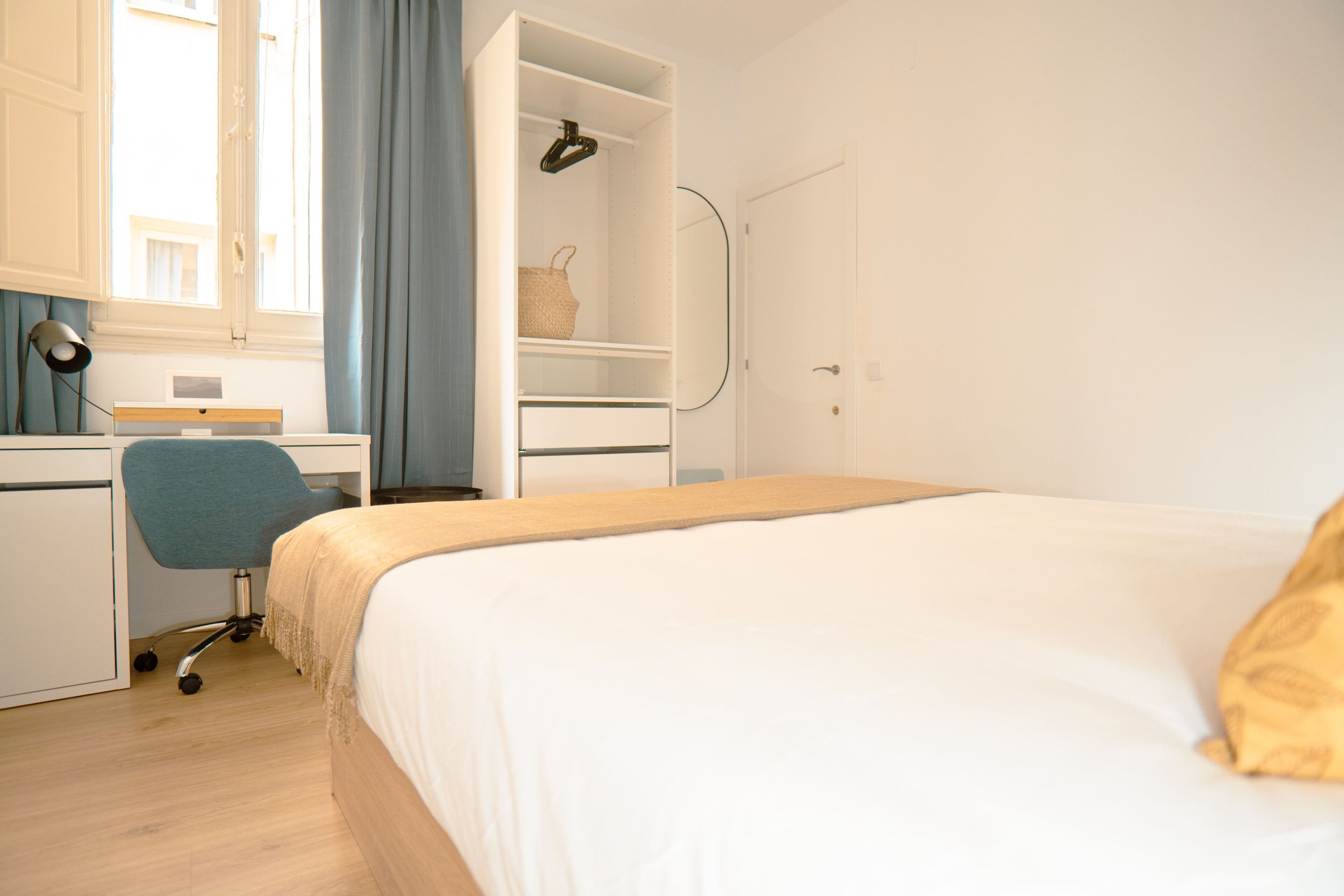 A bedroom with a bed, a desk, a chair, a wardrobe, and a window with curtains.