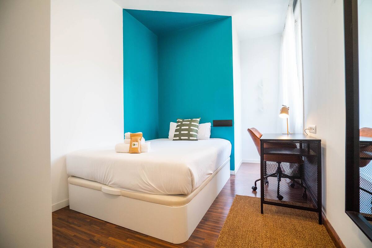 A bedroom with a bed, a desk, and a chair.