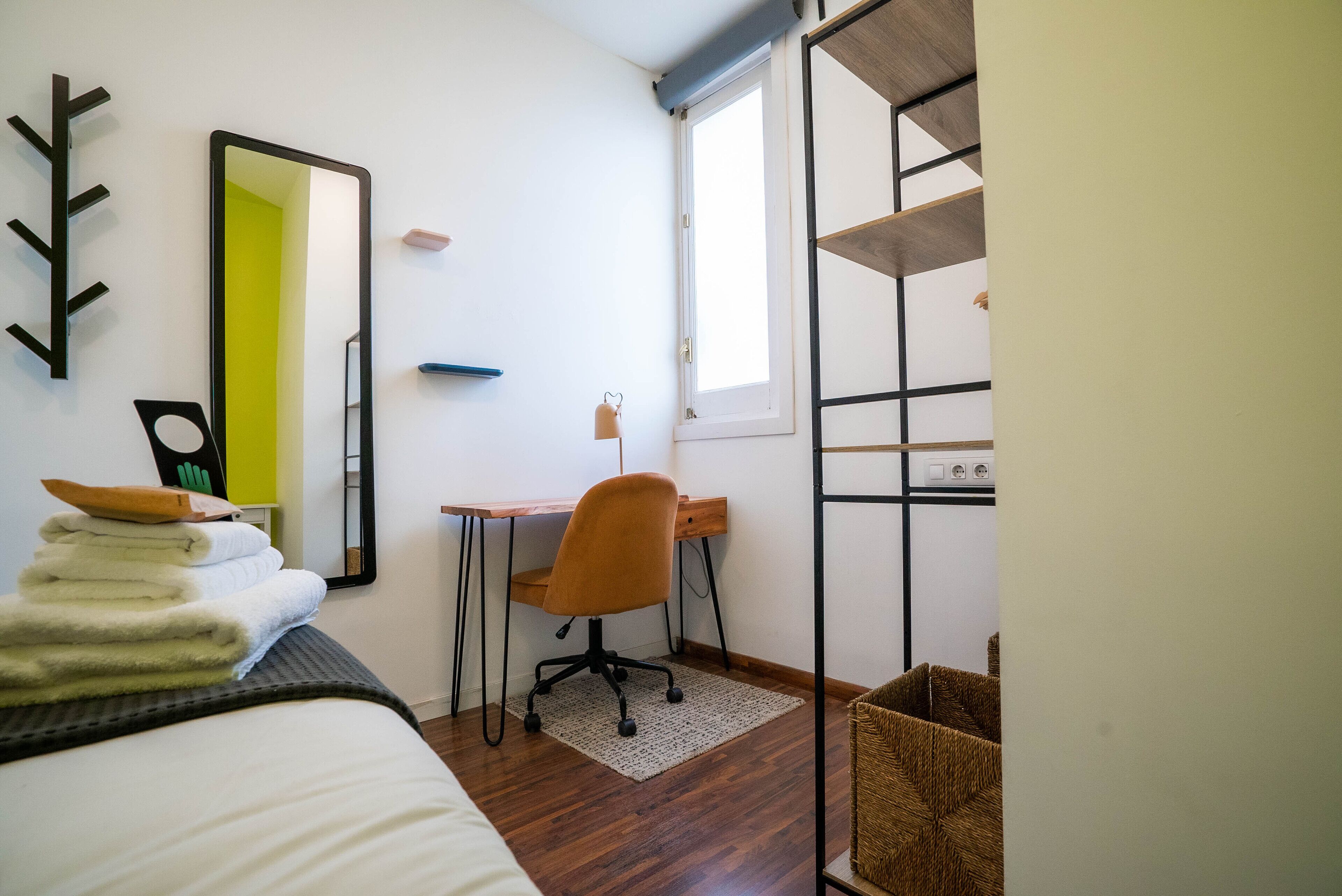 Ein Schlafzimmer mit Bett, Schreibtisch, Stuhl, Spiegel und Fenster.