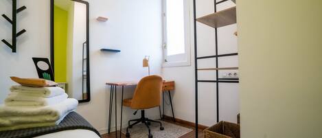 A bedroom with a bed, a desk, a chair, a mirror, and a window.
