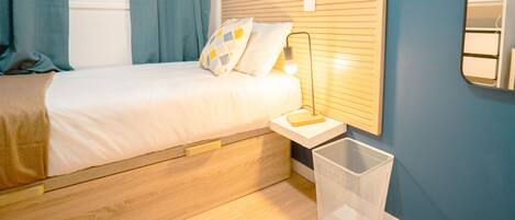 A bedroom with a bed, a nightstand, a lamp, and a wall with a blue mural.