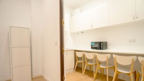 A kitchen with white cabinets, a microwave, and four wooden chairs. - Live It Gran Via (Madrid)