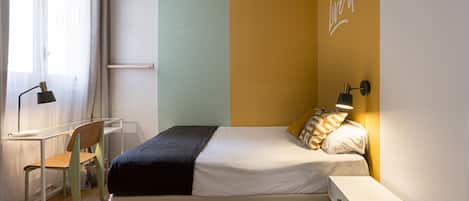 A bedroom with a bed, bedside table, lamp, chair, and a desk.