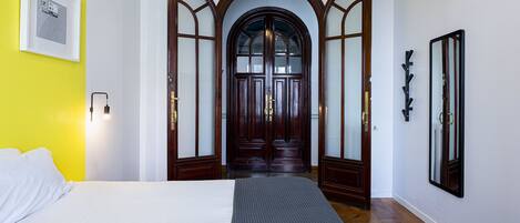 Une chambre d’hôtel avec un lit, une porte en bois dotée de panneaux de verre, un luminaire fixé au mur et un tableau encadré.