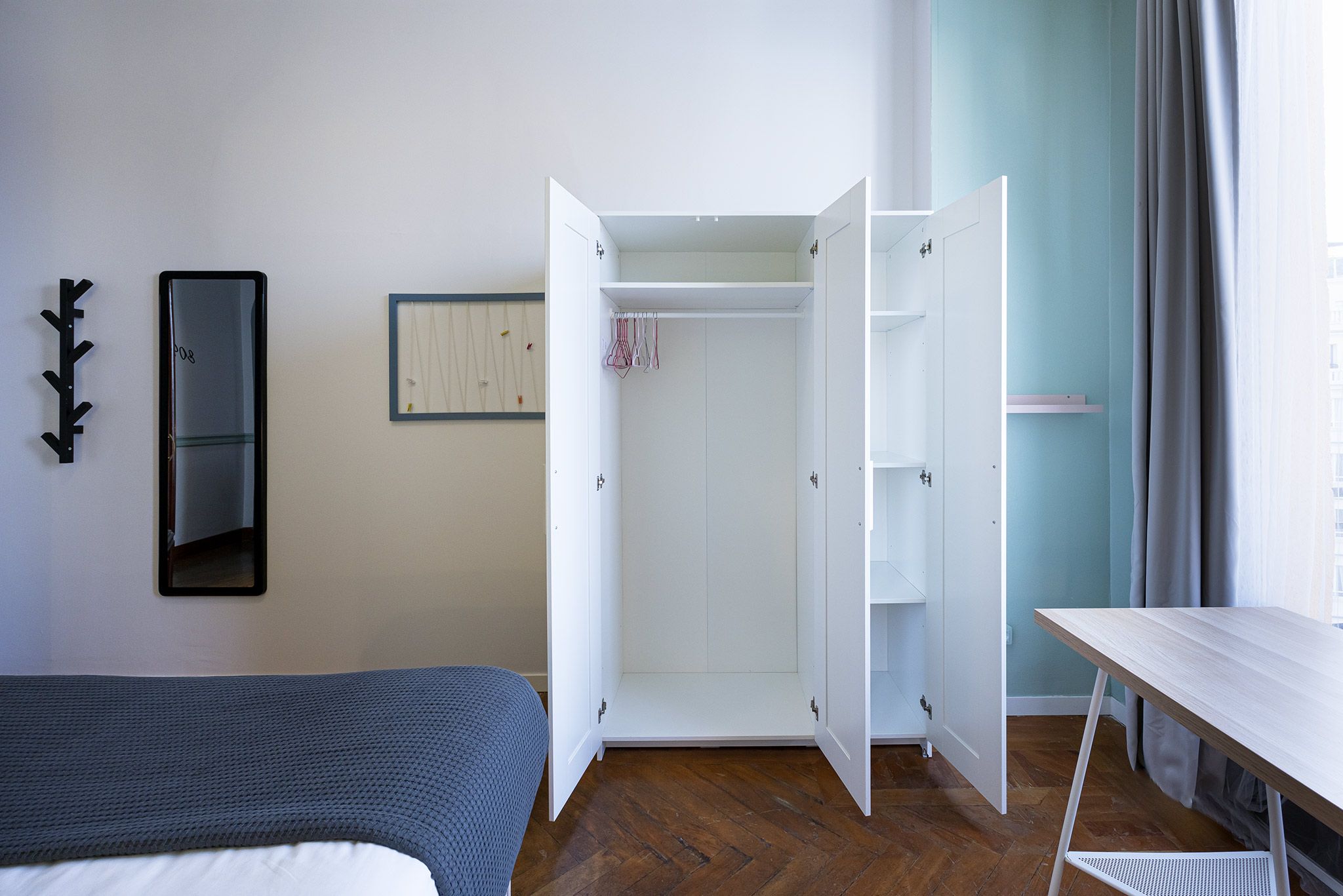 A bedroom with a bed, a wardrobe, a desk, and a mirror.