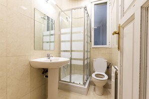 A bathroom with a glass-enclosed shower, a sink, and a toilet. - Live It Gran Via (Madrid)