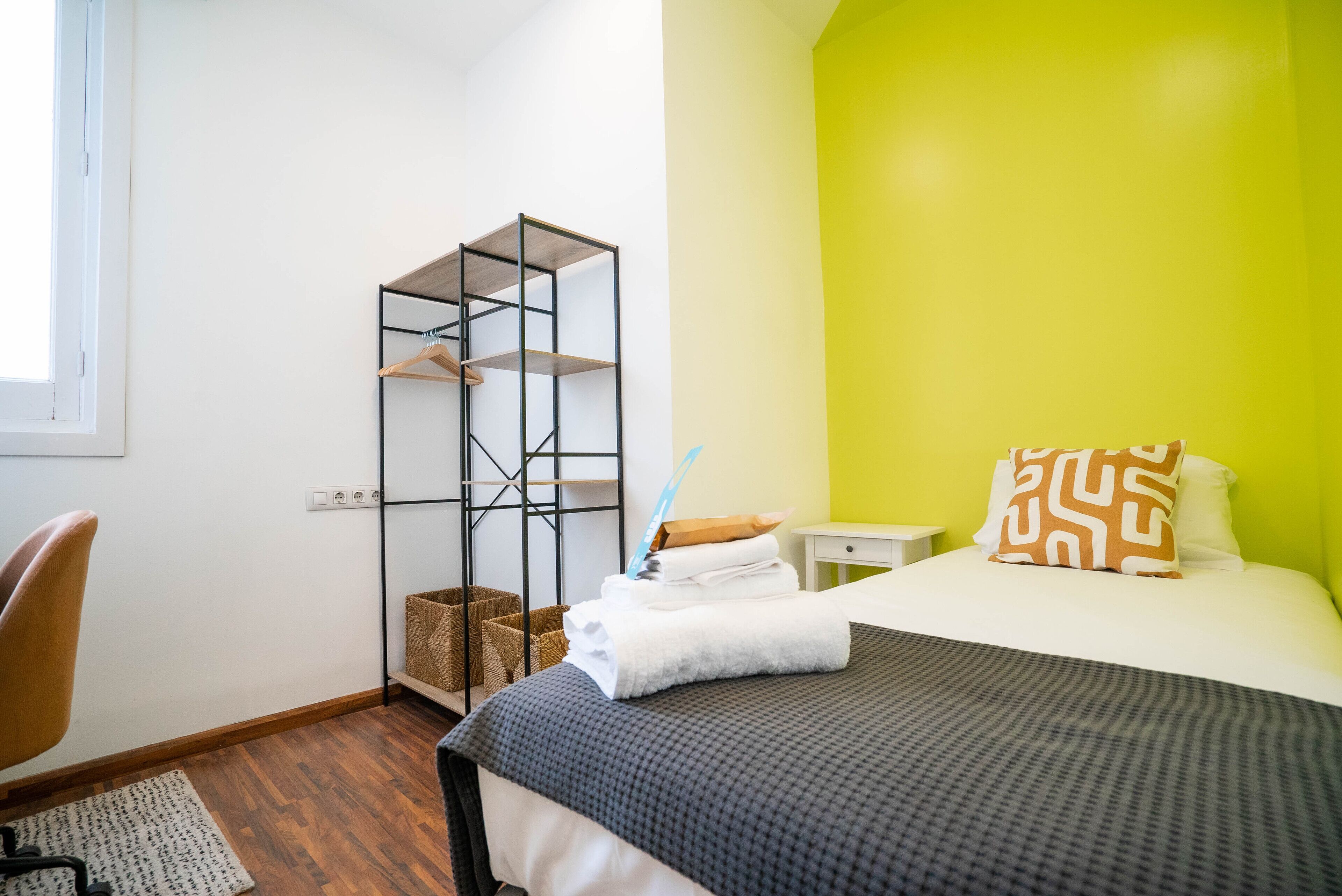 Un dormitorio con cama, escritorio, silla, estante y ventana.