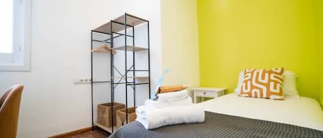 Un dormitorio con cama, escritorio, silla, estante y ventana.