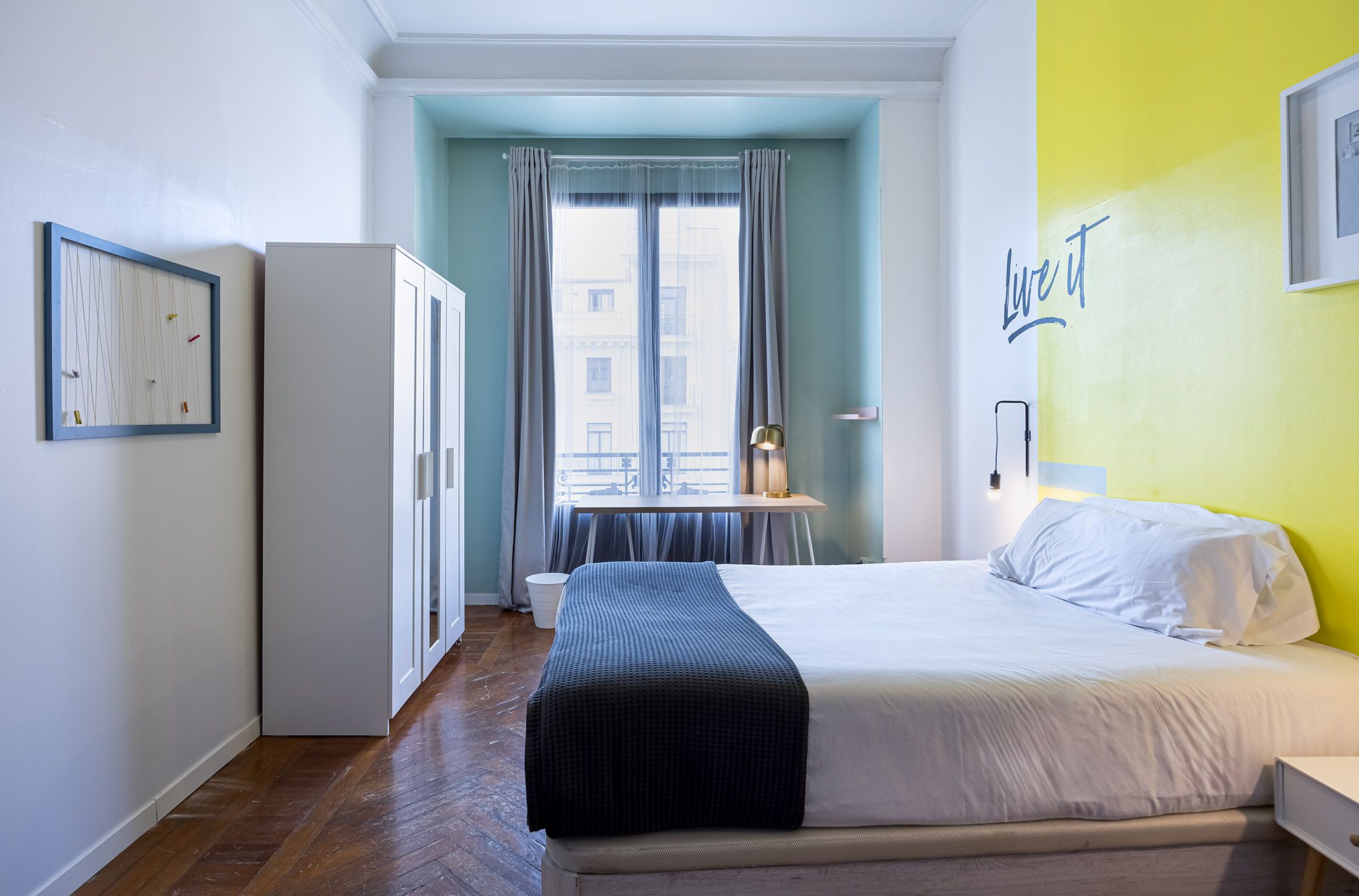 Une chambre à coucher comprenant un lit, une table de chevet, une armoire, une fenêtre avec des rideaux et un mur orné d’une citation inspirante.