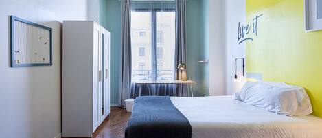 Une chambre à coucher comprenant un lit, une table de chevet, une armoire, une fenêtre avec des rideaux et un mur orné d’une citation inspirante.