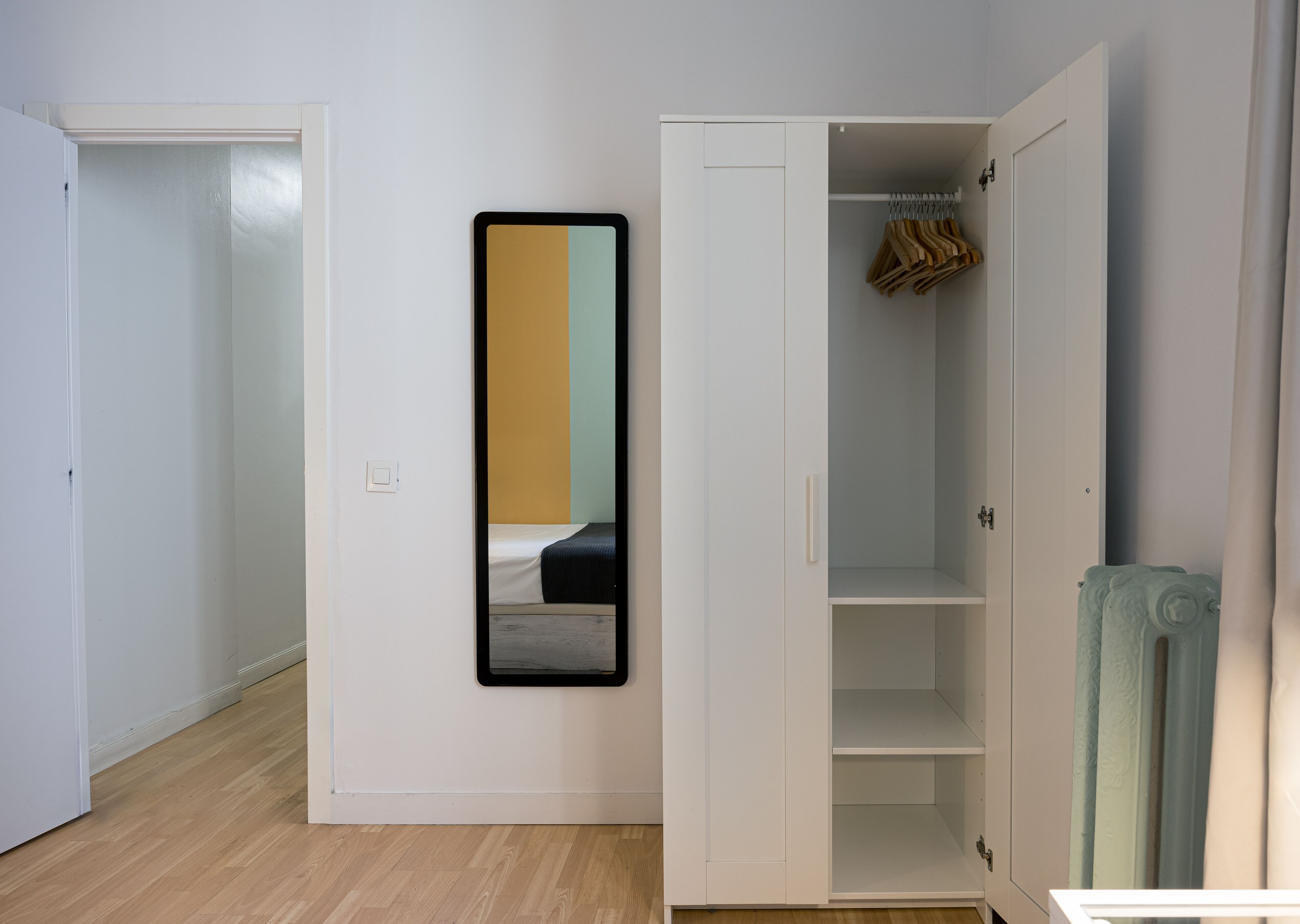 Una stanza con un armadio bianco, uno specchio e un letto.