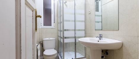 Un baño con inodoro, ducha con mampara de vidrio y lavamanos.