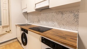 A compact kitchen with a washing machine, a dishwasher, and a wooden countertop. - Live It Gran Via (Madrid)