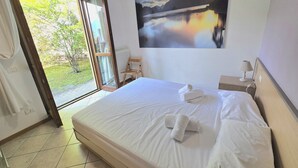 Ein Hotelzimmer mit einem Bett, einem Bild von einem See, einem Sessel und Blick durch die Tür.