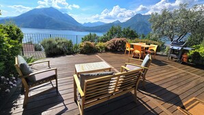 Eine Holzterrasse mit Gartenmöbeln, einem Grill und Blick auf Berge und einen See.