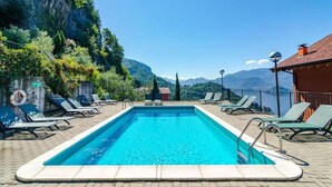 Ein rechteckiger Pool mit klarem, blauem Wasser, umgeben von Liegestühlen und Blick auf Berge.