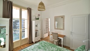 A bedroom with a bed, a dresser, a chair, a desk, a mirror, and a window with curtains.
