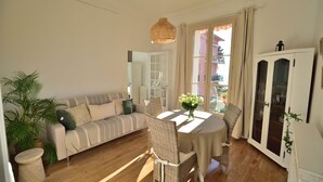A room with a sofa, dining table, chairs, a hanging light fixture, and a cabinet.